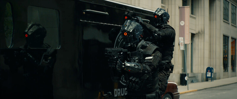 Two policemen in full body armor hold guns and ride on the side of a truck in 'Code 8'