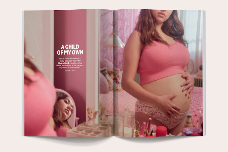 Pregnant woman in a pink top and floral underwear stands in a pink bedroom, holding her belly. A mirror reflects her face. The room has feminine decor and beauty products on a vanity, evoking a personal, intimate atmosphere.