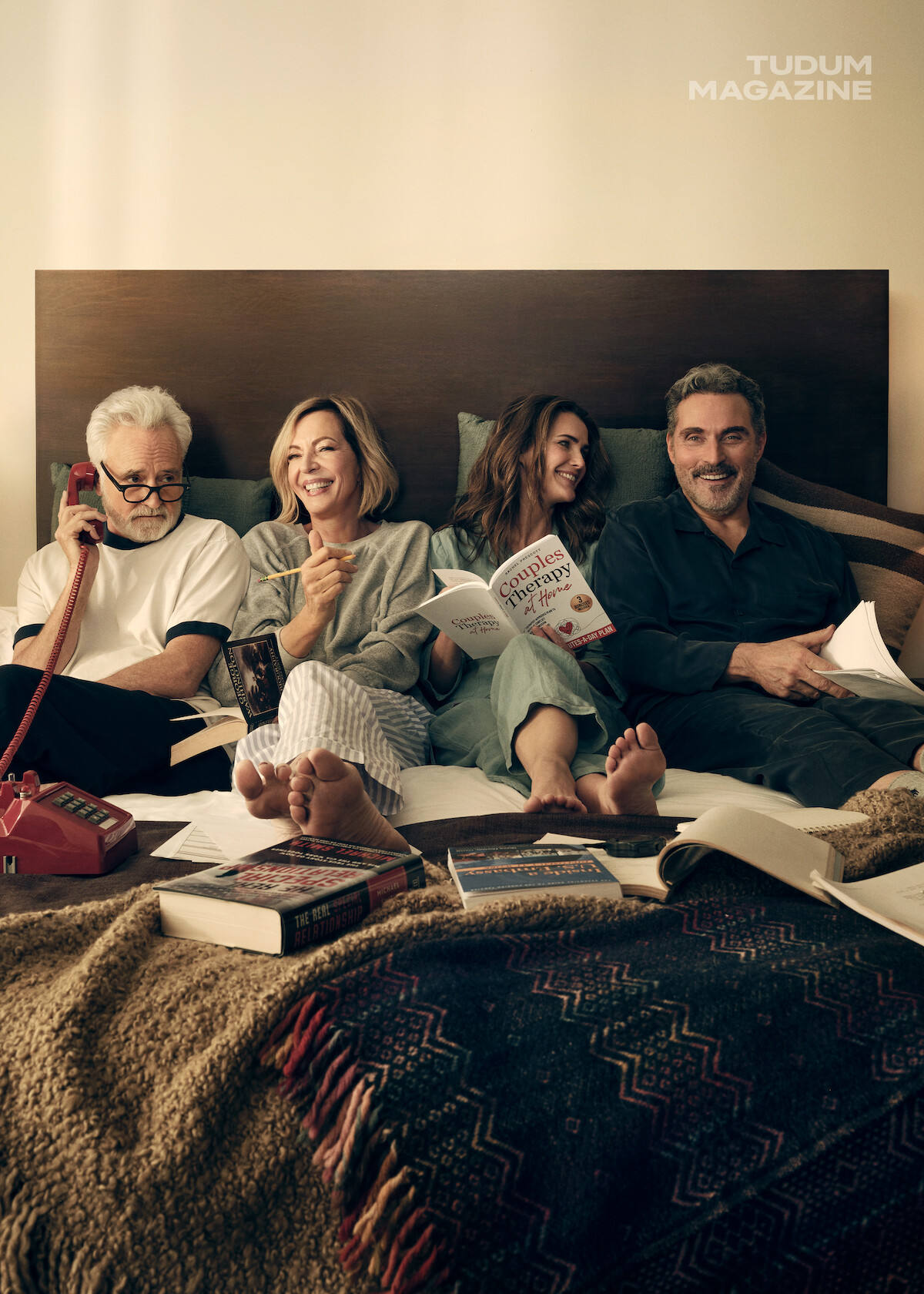 Bradley, Allison, Keri e Rufus sentados em uma cama cheia de livros, rindo