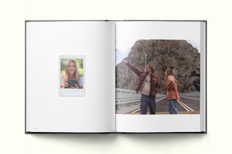 Open photo book with one page showing a woman smiling with a camera, outdoors, and the other page showing two people standing on a road pointing at a large rocky mountain in the background.