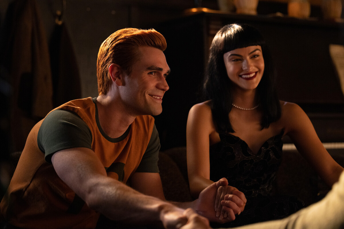 K.J. Apa as Archie Andrews and Camila Mendes as Veronica Lodge sit together smiling in Season 7 of ‘Riverdale.’