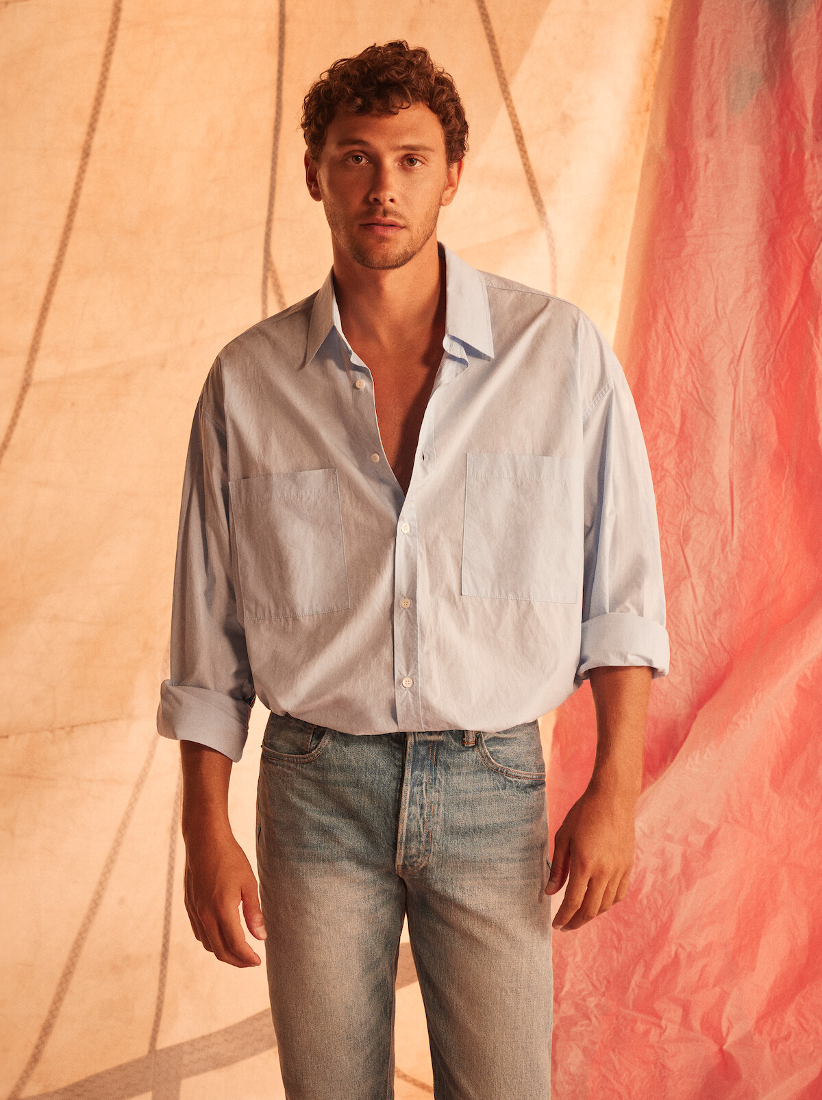 Cooper Koch wearing a blue button down and jeans, posing looking directly to camera in front of a sail.