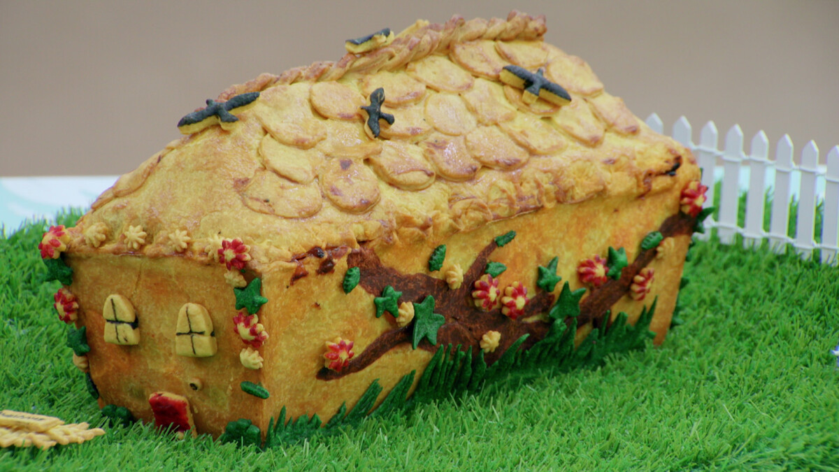 A pie baked in the shape of a cottage, adorned with pastry flowers, birds and other decorations