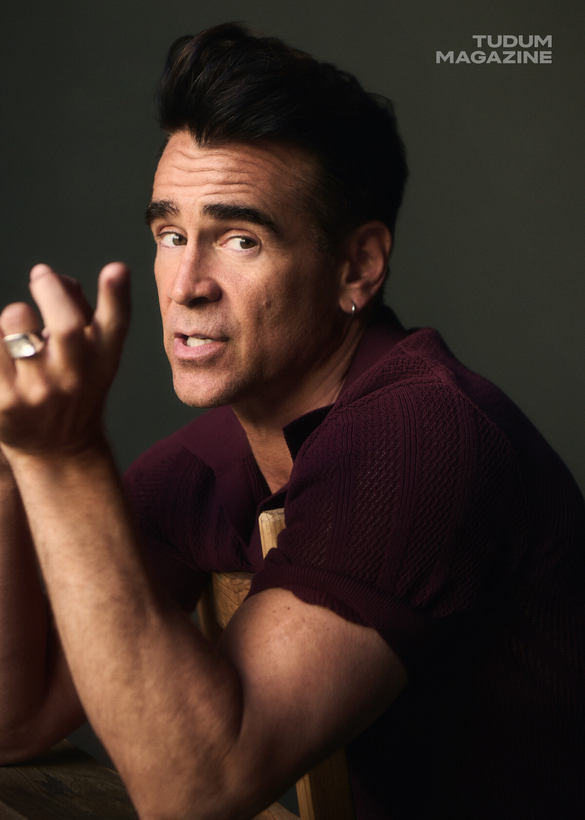 Colin Farrell points in the direction of the camera while wearing a maroon polo.