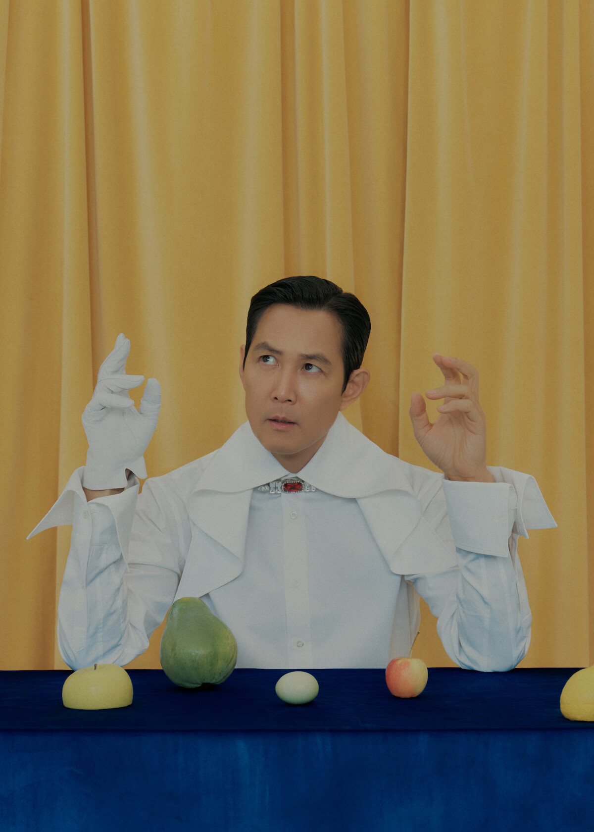 Lee Jung-jae of ‘Squid Game’ sits at a table with pieces of fruit and an egg in front of him.