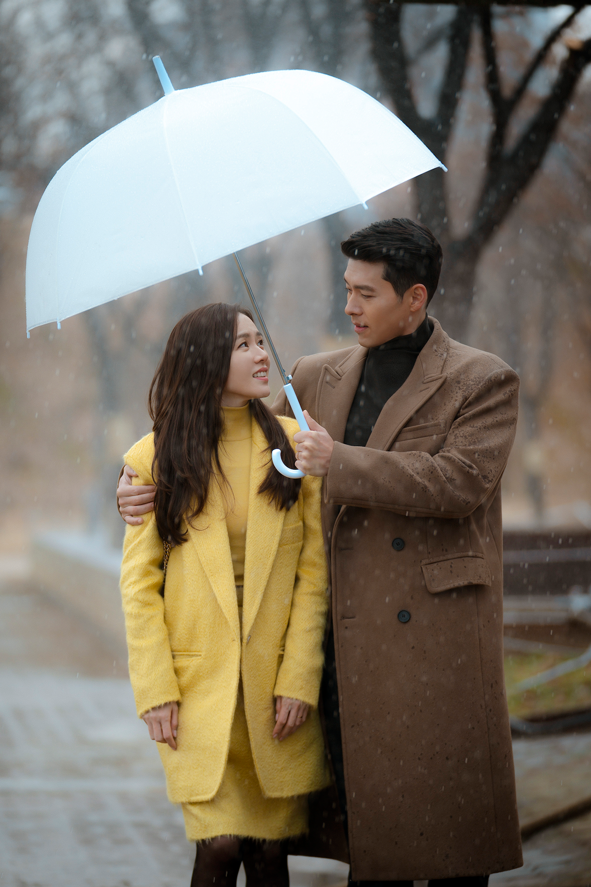 Um homem e uma mulher asiáticos se abraças debaixo de um guarda-chuva