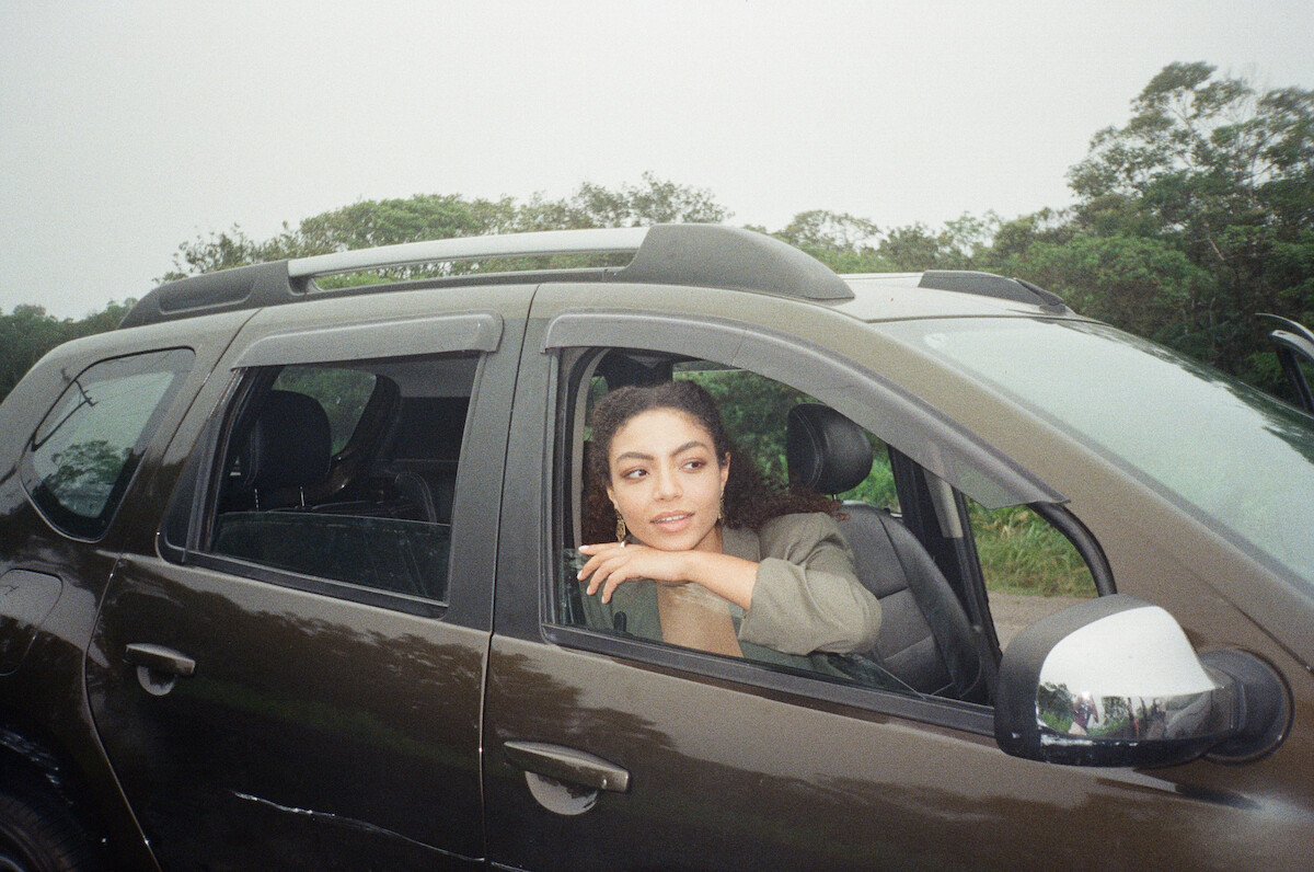 Atriz Any Gabrielly apoia o braço na janela dianteira de um carro