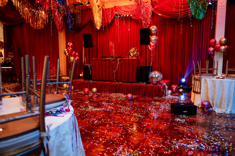 Um salão em tons de vermelho onde uma festa acabou de terminar tem papel picado e adereços brilhantes por toda parte