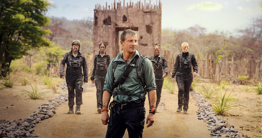 Bear Grylls stands in front of four people on a rocky path. 