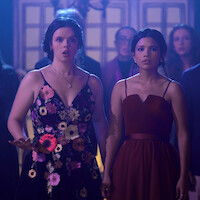 Ellie O’Brien as Grace and Nikki Rodriguez as Jackie wearing dresses in a crowd in 'My Life with the Walter Boys' Season 2.
