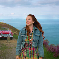 Ed Speleers and Lindsay Lohan walk along a scenic coastal path with the ocean behind them in Irish Wish.