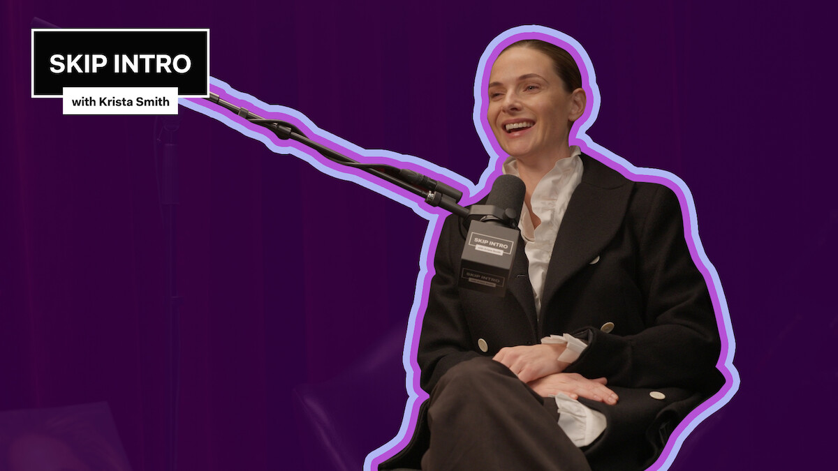 Rebecca Ferguson sorri enquanto fala ao microfone em um estúdio de podcast. No canto, aparece o logotipo ‘SKIP INTRO with Krista Smith’ sobre um fundo roxo-escuro.