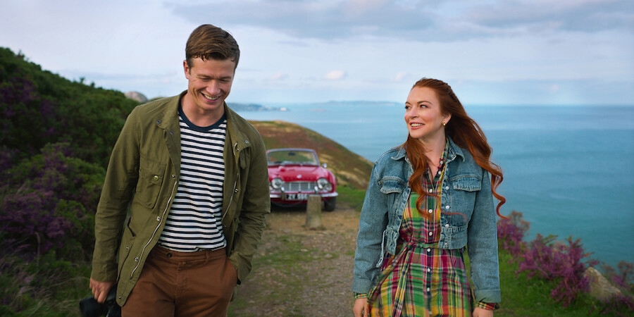 Ed Speleers and Lindsay Lohan walk along a scenic coastal path with the ocean behind them in Irish Wish.