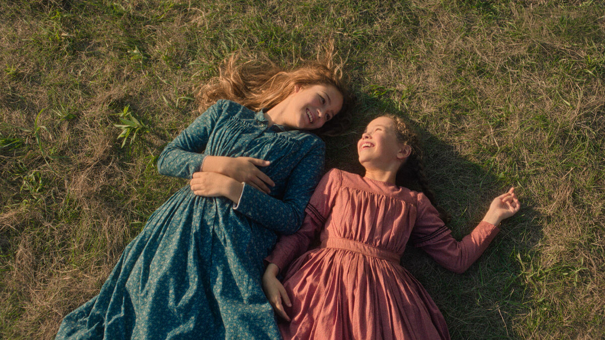 Two girls lay down in a field and laugh.