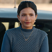Nikki Rodriguez como Jackie de blusa azul, parada ao lado de um carro na temporada 2 de ‘Minha Vida com a Família Walter’.