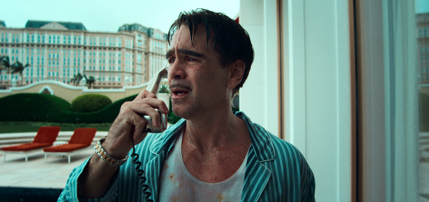 A distressed man in pajamas talks on a corded phone at a luxurious hotel with a resort pool and lounge chairs outside, creating a tense, dramatic mood.