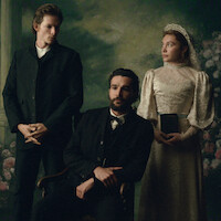 Three people in vintage formal attire pose indoors against a painted floral backdrop; a seated man in a suit is flanked by a standing man and woman in a lace dress with a tiara, holding a book, evoking an old-fashioned, solemn portrait.