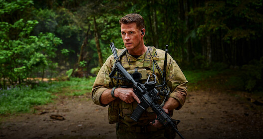 Liam Hemsworth as Sgt. JJ Kinney walks through a jungle holding a gun in 'Land of Bad'