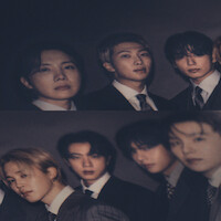 Seven young men in formal suits pose together indoors with a dark, moody background; the image is slightly blurred and dimly lit, creating a sophisticated group portrait atmosphere.