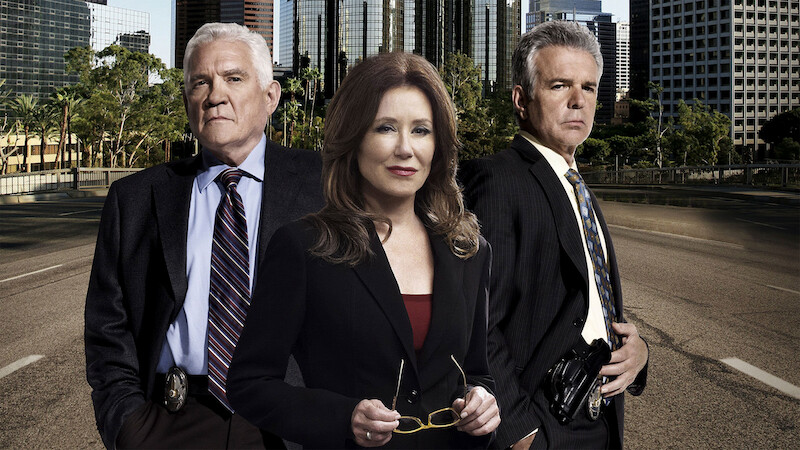 Three serious-looking detectives in suits stand on an empty city street with tall buildings and trees in the background, suggesting an urban law enforcement setting.