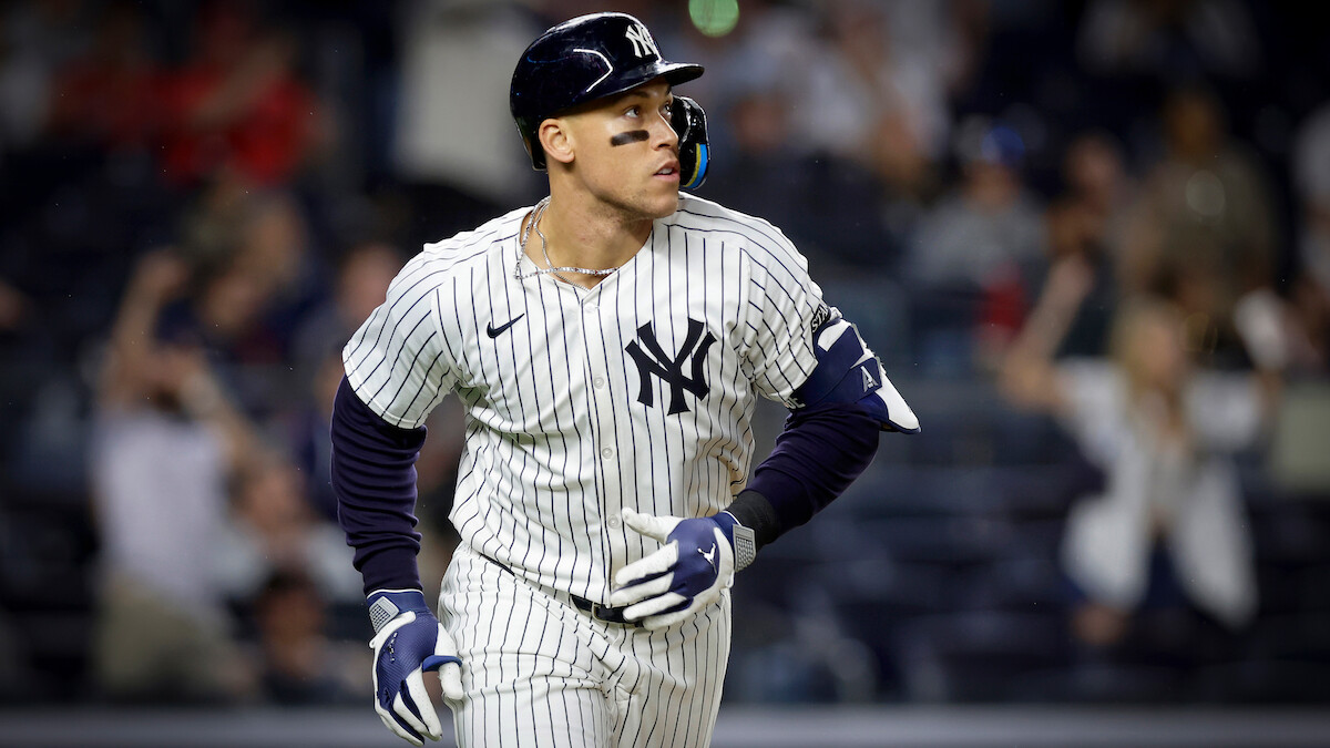 New York Yankees baseball player in pinstripe uniform runs on field during a night game; blurred crowd in the background creates an energetic, competitive atmosphere.