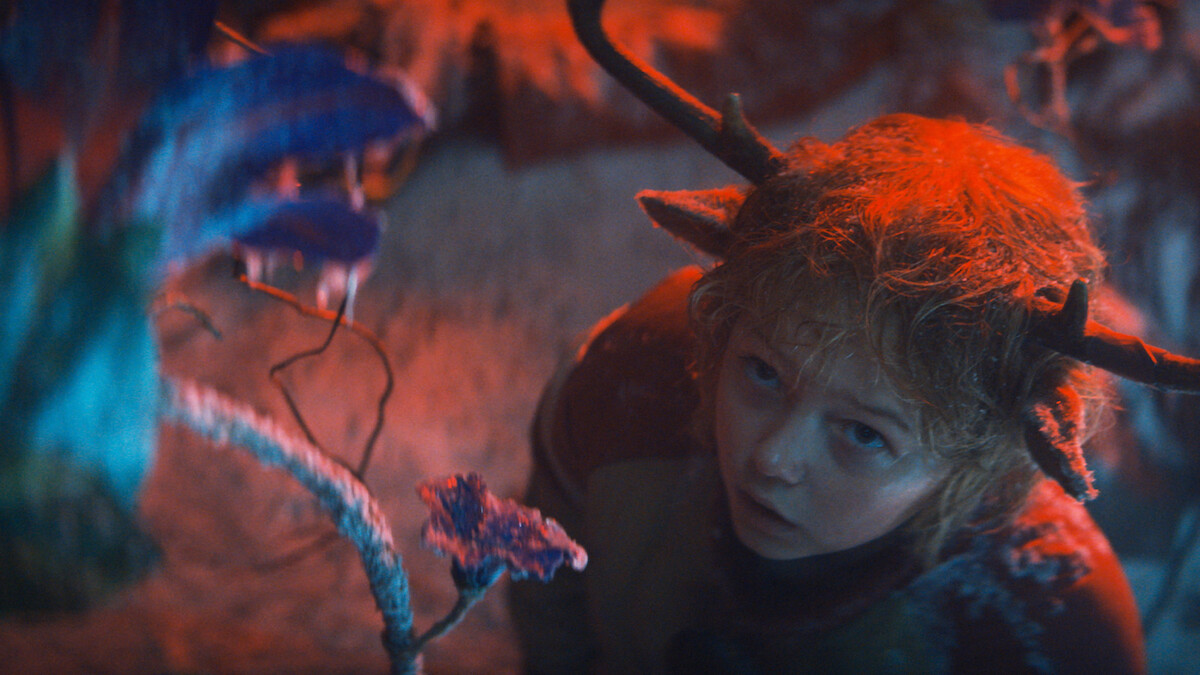 Christian Convery as Gus looks at a purple flower while shrouded in red light in Season 3 of 'Sweet Tooth'