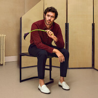 Adam Brody está sentado em um banco segurando uma flor copo-de-leite preta