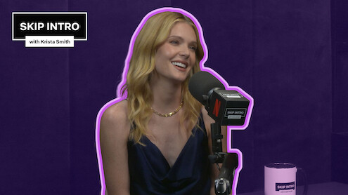 Meghann Fahy smiles and speaks into a “Skip Intro with Krista Smith” microphone against a purple background, with a matching “Skip Intro” mug on the table.