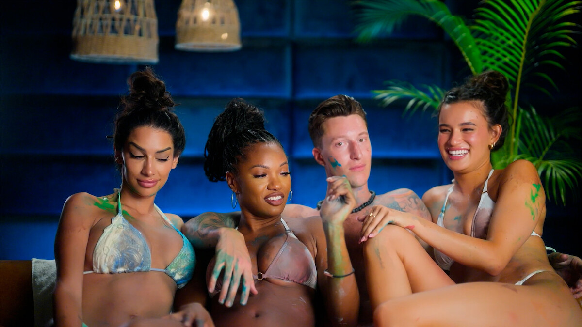 Cast members of 'Temptation Island' in swimsuits covered in body paint sit together on a couch.
