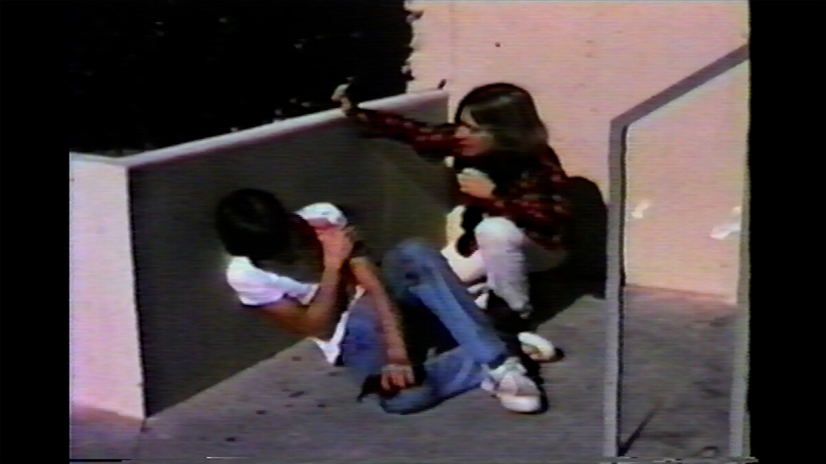 Charlie Sheen and Chris Penn are in a corner outside; one is sitting on the ground with their arm across their chest, while the other crouches nearby, reaching out toward them.