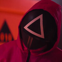 Duas figuras mascaradas com capacetes de esgrima se olham em um ambiente com iluminação vermelha