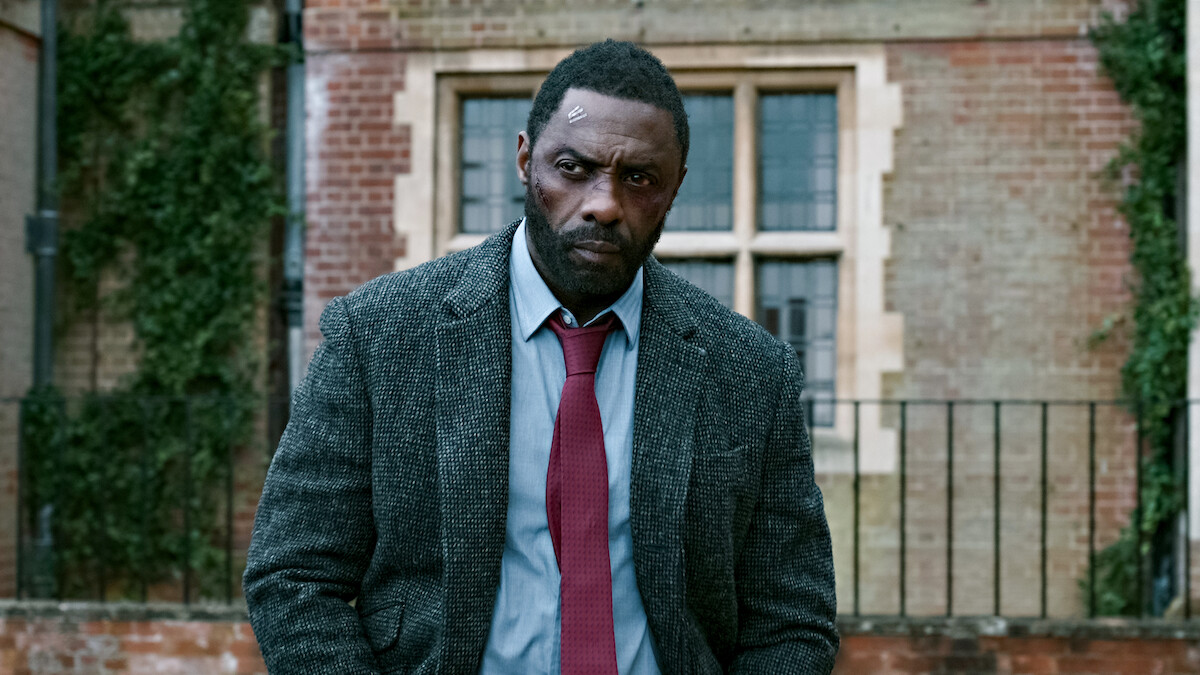 Serious man in a suit with a head injury stands outside a brick building with ivy, giving a tense and somber mood.