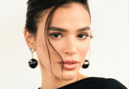 Bruna Marquezine é uma mulher branca, magra, de cabelos escuros e presos, com brincos grandes e veste um vestido preto