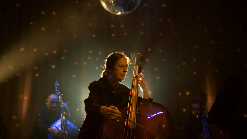 Orin O’Brien playing her double bass on stage under a mirrorball