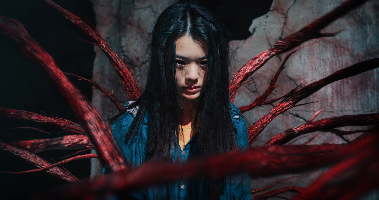 A girl with black eyes and a menacing expressions is shrouded in red rine-like chords 'Sweet Home'