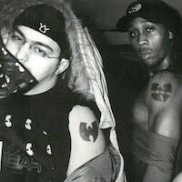 Two men pose in a black and white photo, both displaying Wu-Tang Clan tattoos. One wears a hooded jacket and a face covering, the other is shirtless with a cap, standing in an indoor setting with a serious expression.