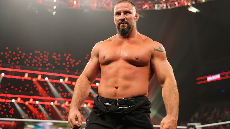 Bron Breakker standing shirtless in a wrestling ring, with bright arena lights and a large audience in the background, during a live professional wrestling event.