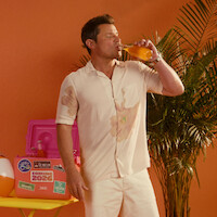 Nick Lachey taking a sip of an orange drink.