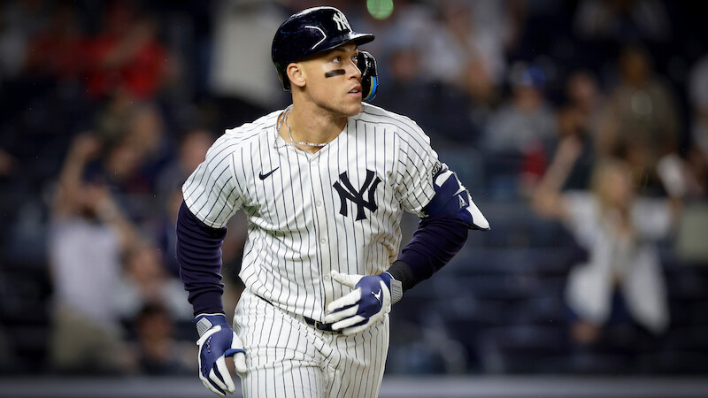 New York Yankees baseball player in pinstripe uniform runs on field during a night game; blurred crowd in the background creates an energetic, competitive atmosphere.