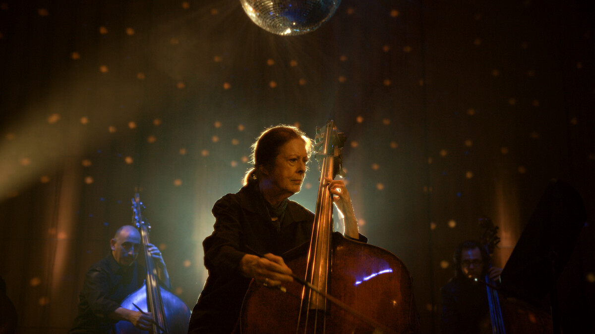 Orin O’Brien playing her double bass on stage under a mirrorball