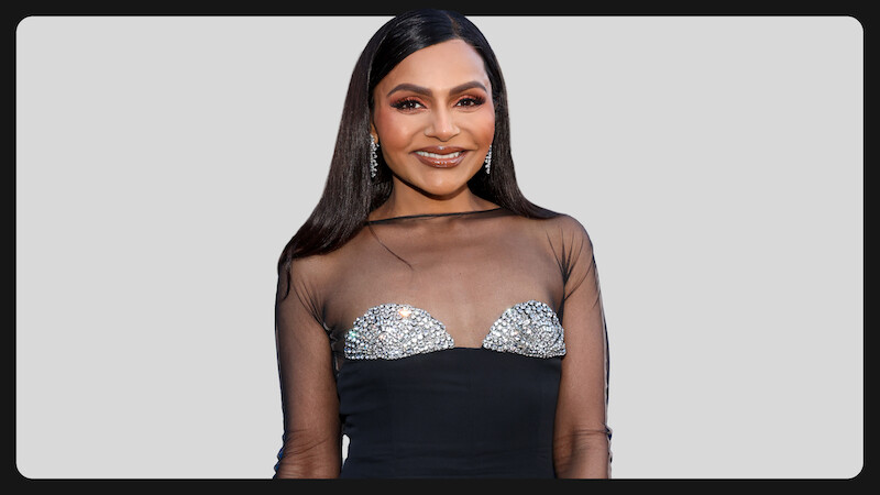 Woman wearing a black dress with sheer top and sparkling embellishments, standing in front of a light gray background, smiling and posing for the camera, formal event setting.
