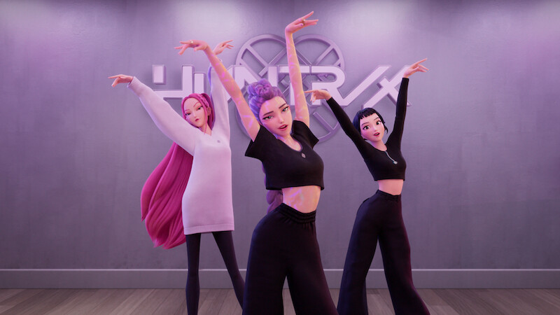 Three animated women in a modern dance studio pose gracefully with raised arms, wearing stylish black and pink outfits, wooden floor, and a wall with the "HUNTR/X" sign in the background.