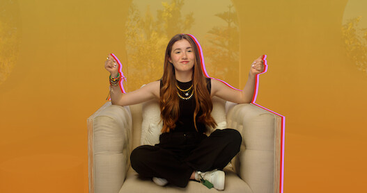 Lucy Paez snaps her hands while sitting casually on an oversize chair.