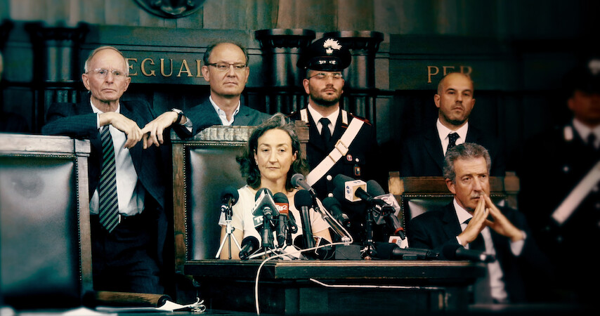 A woman sits in front of a podium with several microphones in 'The Yara Gambirasio Case: Beyond Reasonable Doubt'