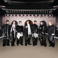 V, JIN, SUGA, RM, JUNG KOOK, J-HOPE, and JIMIN dressed in fashionable black and white outfits stand outdoors at night in front of an ornate, traditional East Asian building with arches and a large decorative roof.