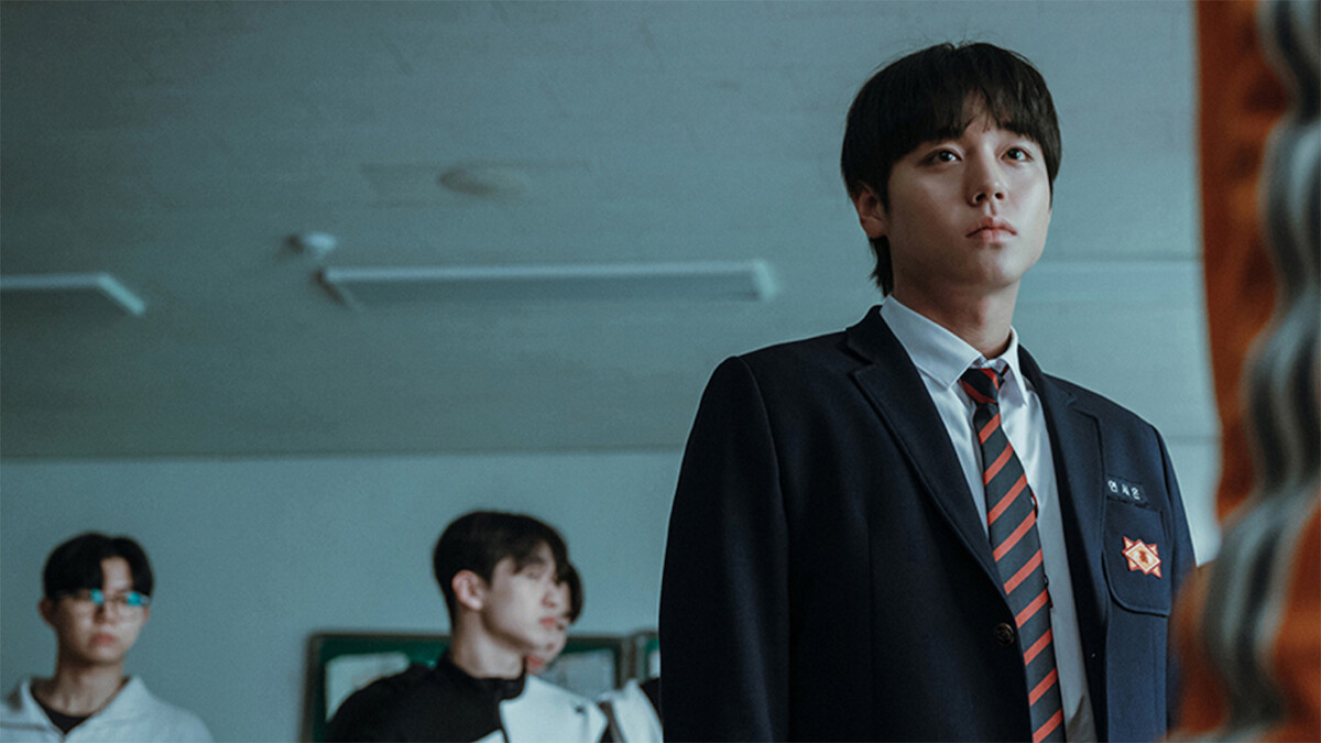 In a classroom, Park Ji-hoon wears a school uniform and stars blankly ahead.