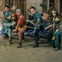 Four young warriors in fantasy costumes face an opponent producing blue energy in an ancient, dimly lit building with oriental decor and scattered debris, suggesting a tense magical battle scene.
