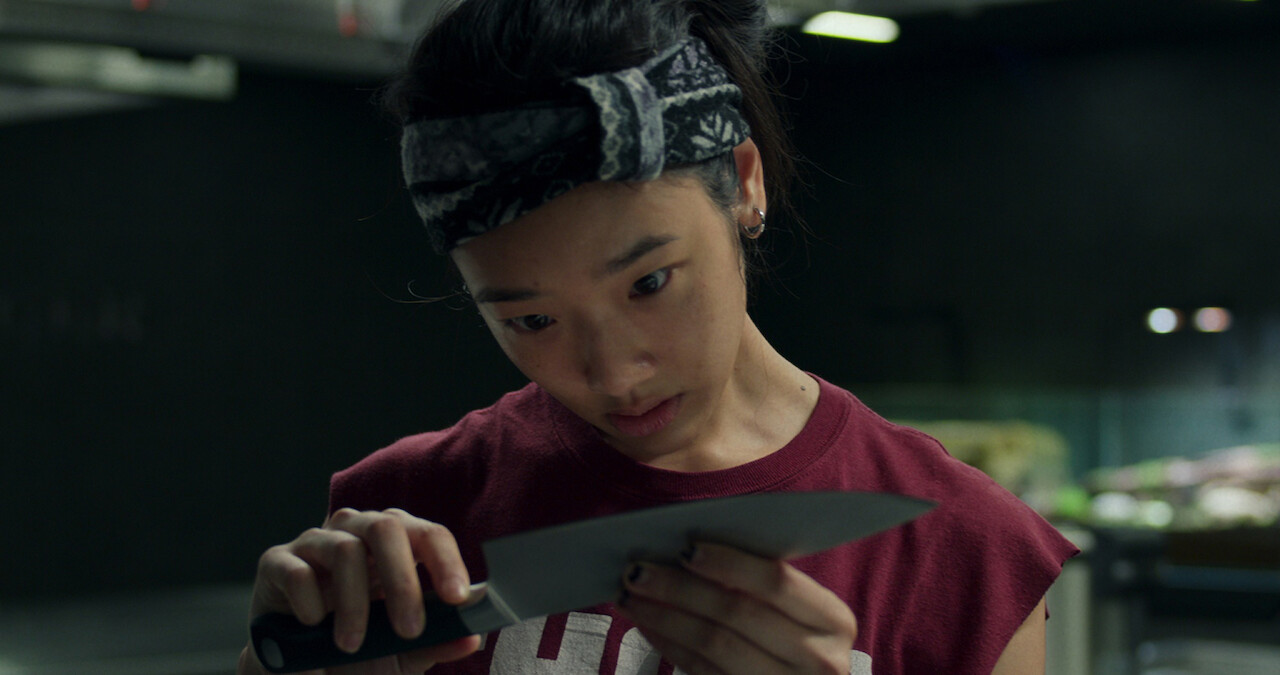 A young woman looks down at a knife she holds in her hand in a still from the movie 'Hunger.'