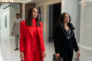 Crystle Stewart as Mallory and Taylor Polidore Williams as Kimmie in business attire, one in a red suit and the other in a black suit, walk confidently down a modern office hallway, with a man in a grey suit walking behind them.