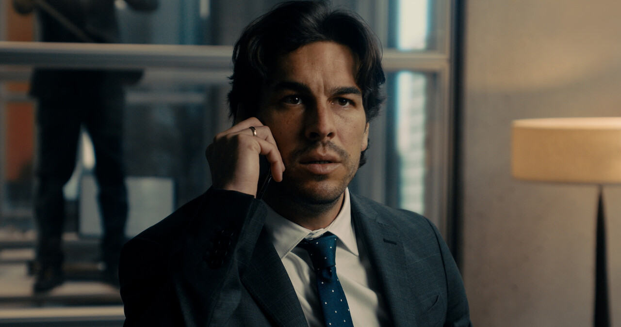 Mario Casas wears a suit and tie while on a phone call in a still image from the film 'Bird Box Barcelona.'